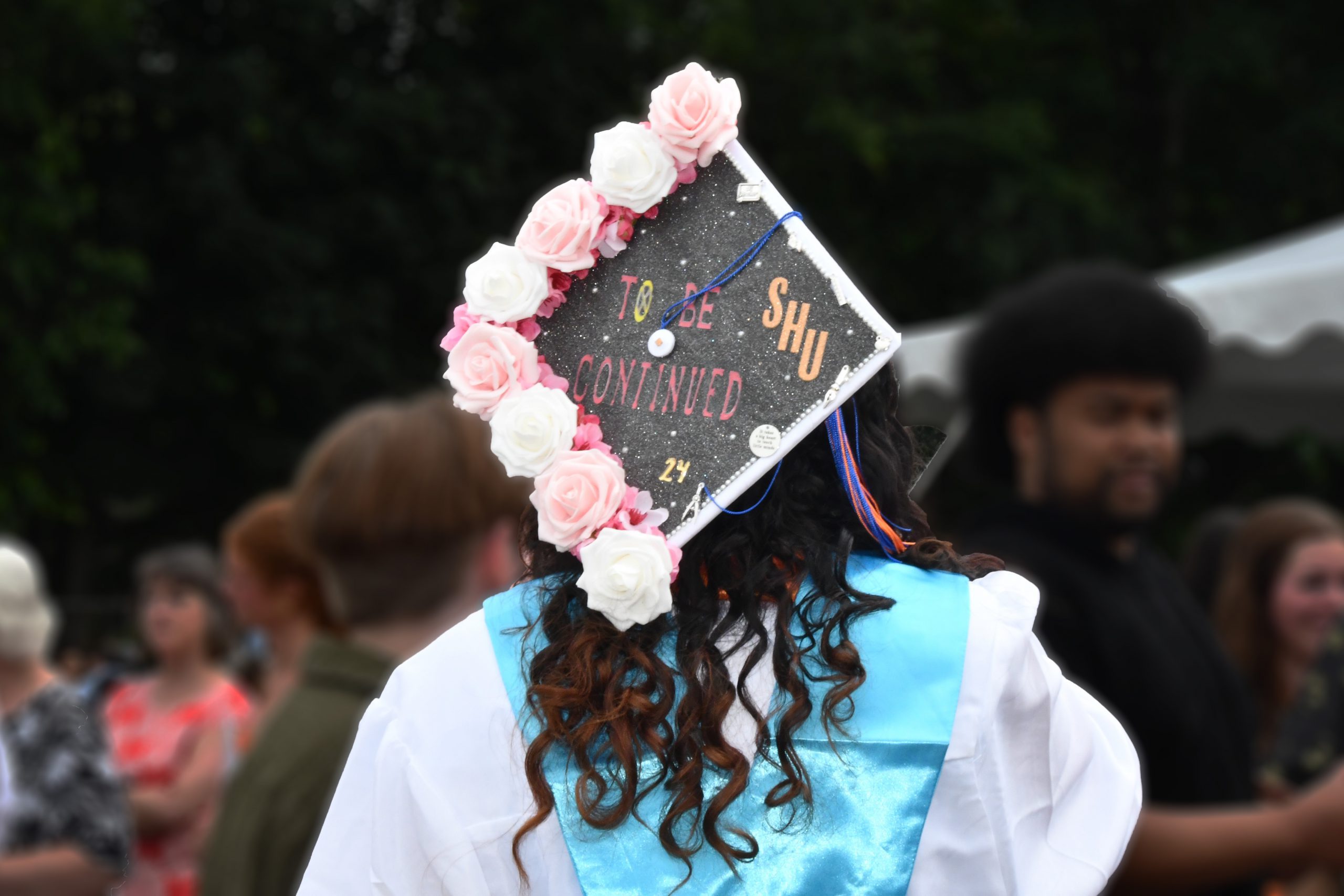 student wears graduation cap with flowers. It says "to be continued SHU"