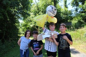 students pose with contraption and group for egg drop. Their work includes plastic bags and balloons as a parachute for the egg attached to a box.