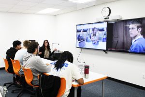 four students in the classroom and one on the screen (distance learner) engage in a Spanish 4 class