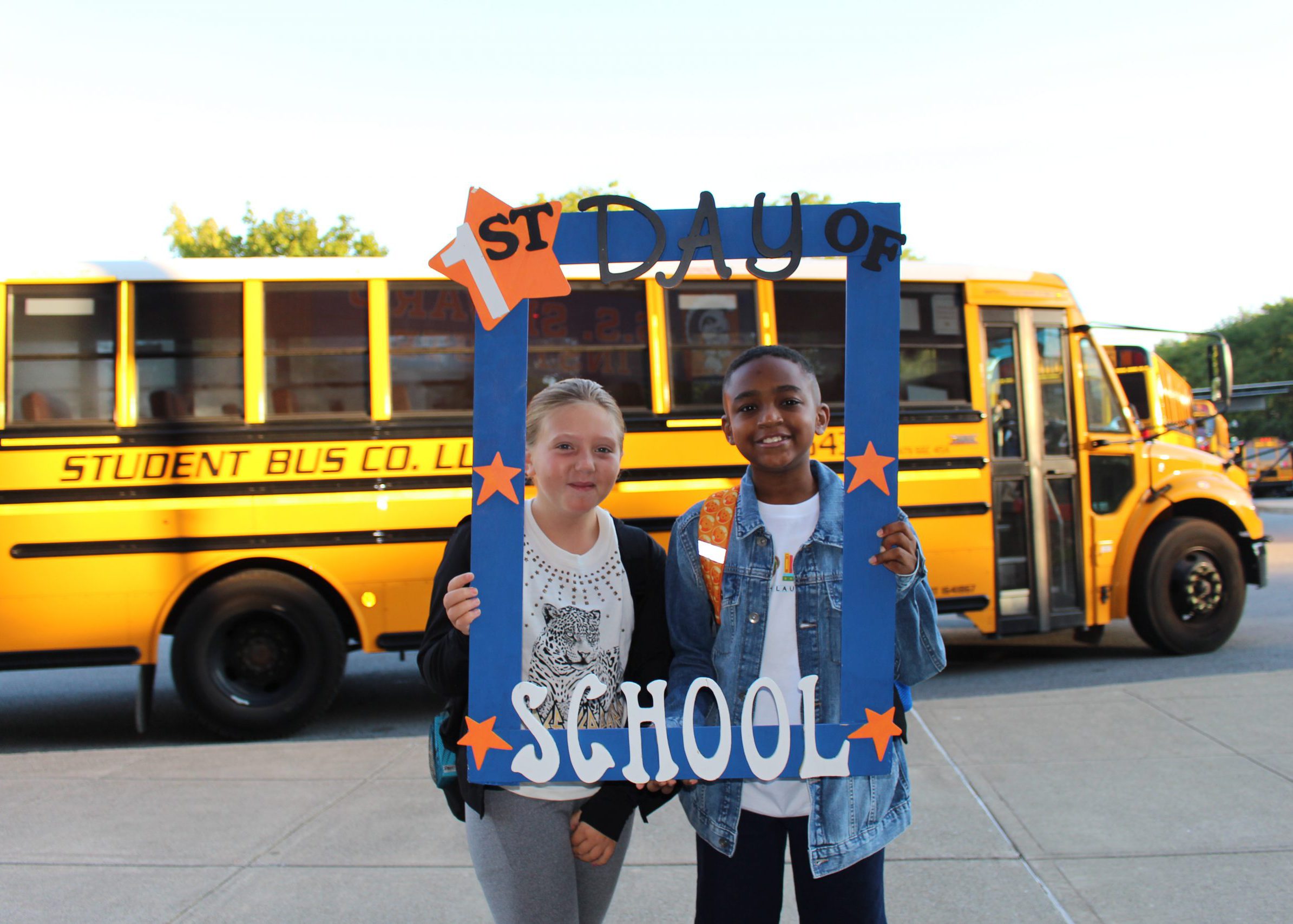 students smile from inside large frame that says "first day of school"