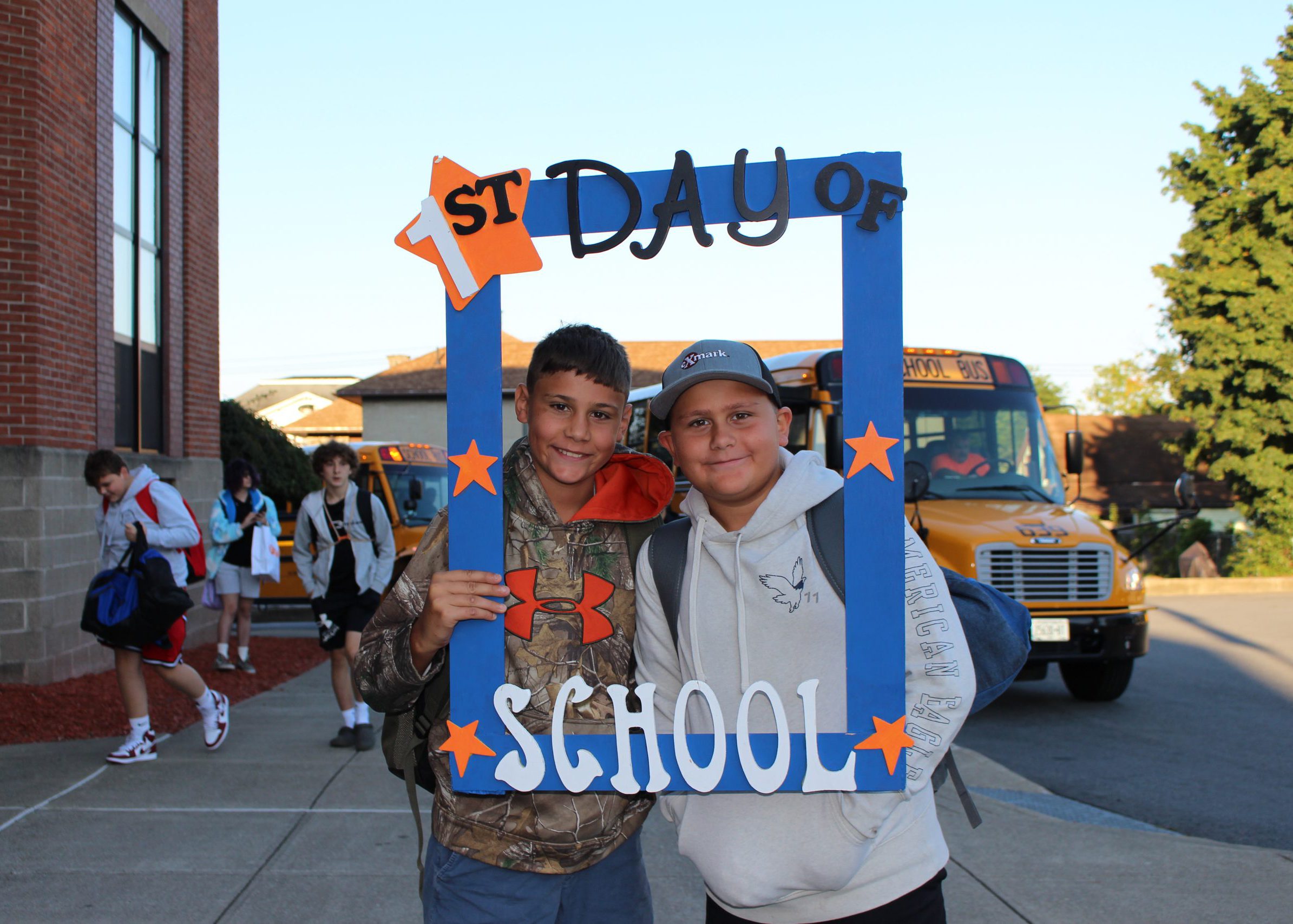 students smile from inside large frame that says "first day of school"