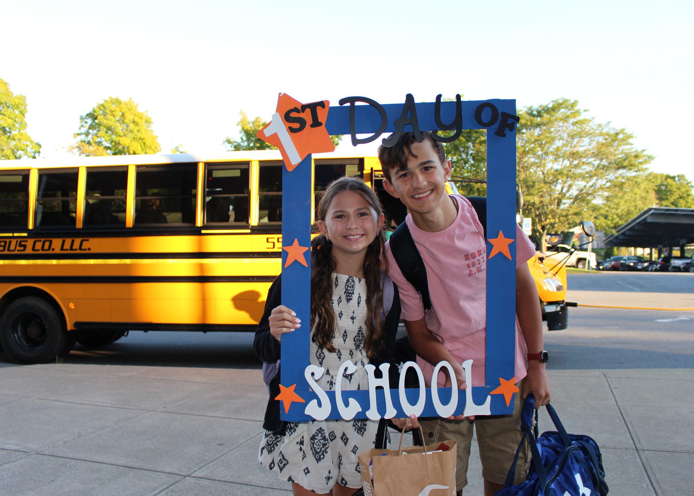 students smile from inside large frame that says "first day of school"