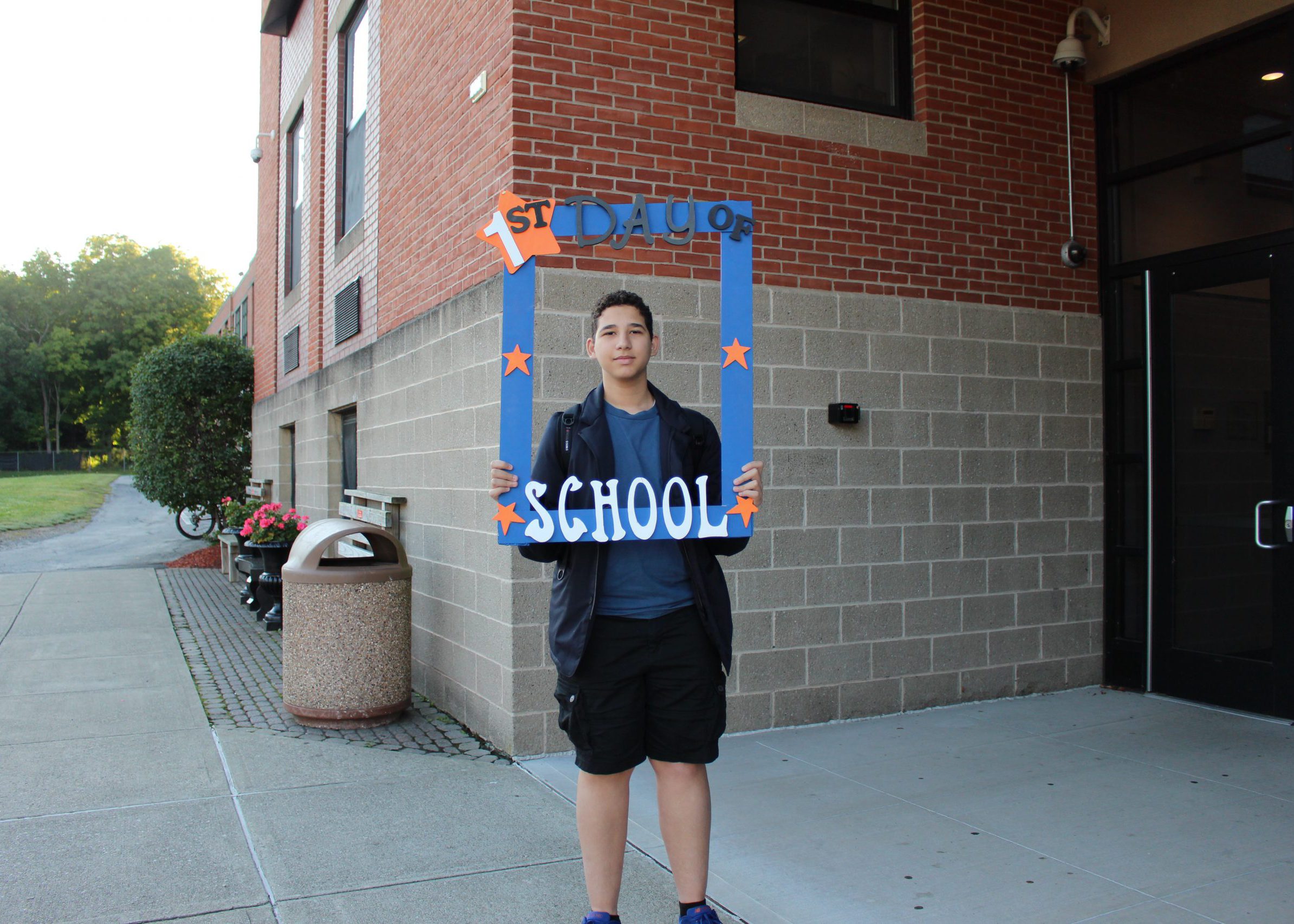 student smiles from inside large frame that says "first day of school"