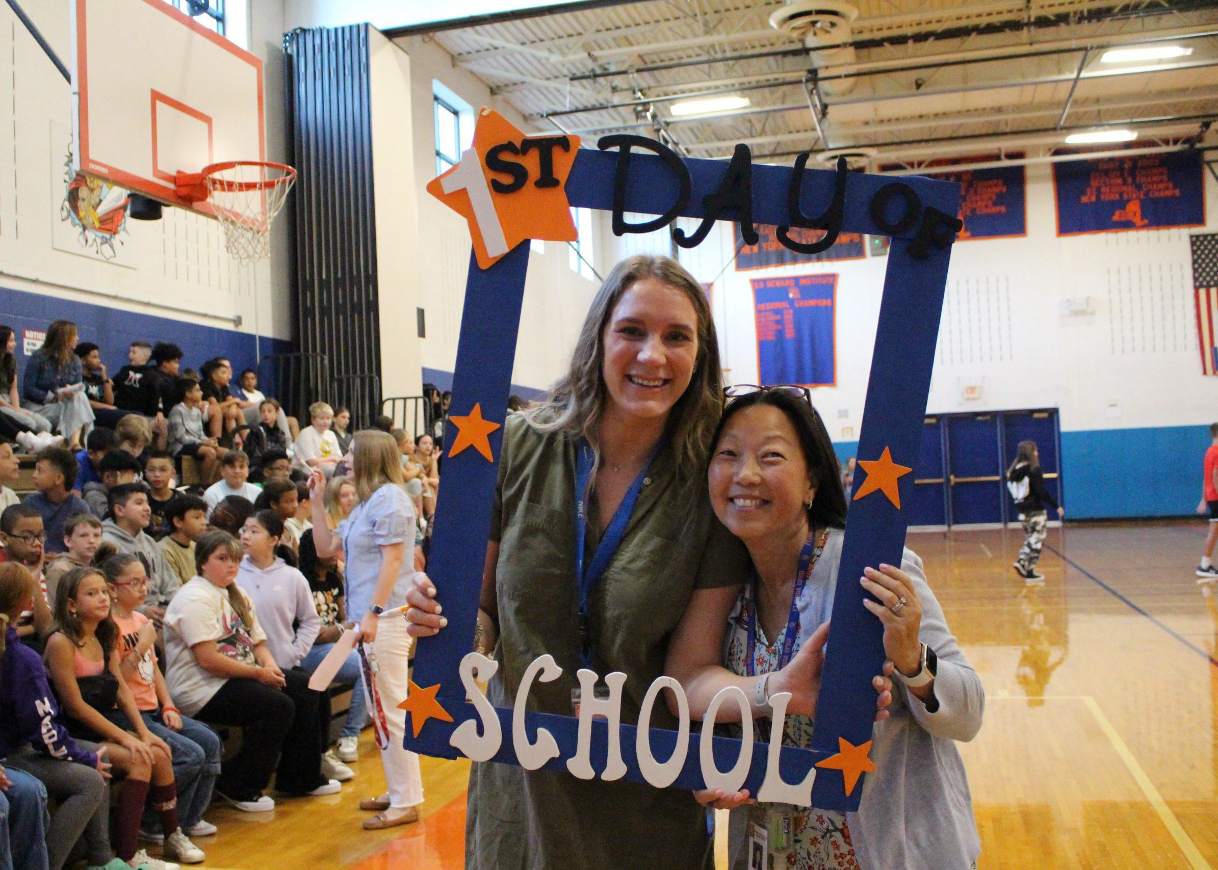 two staff members smile from inside large frame that says "first day of school"