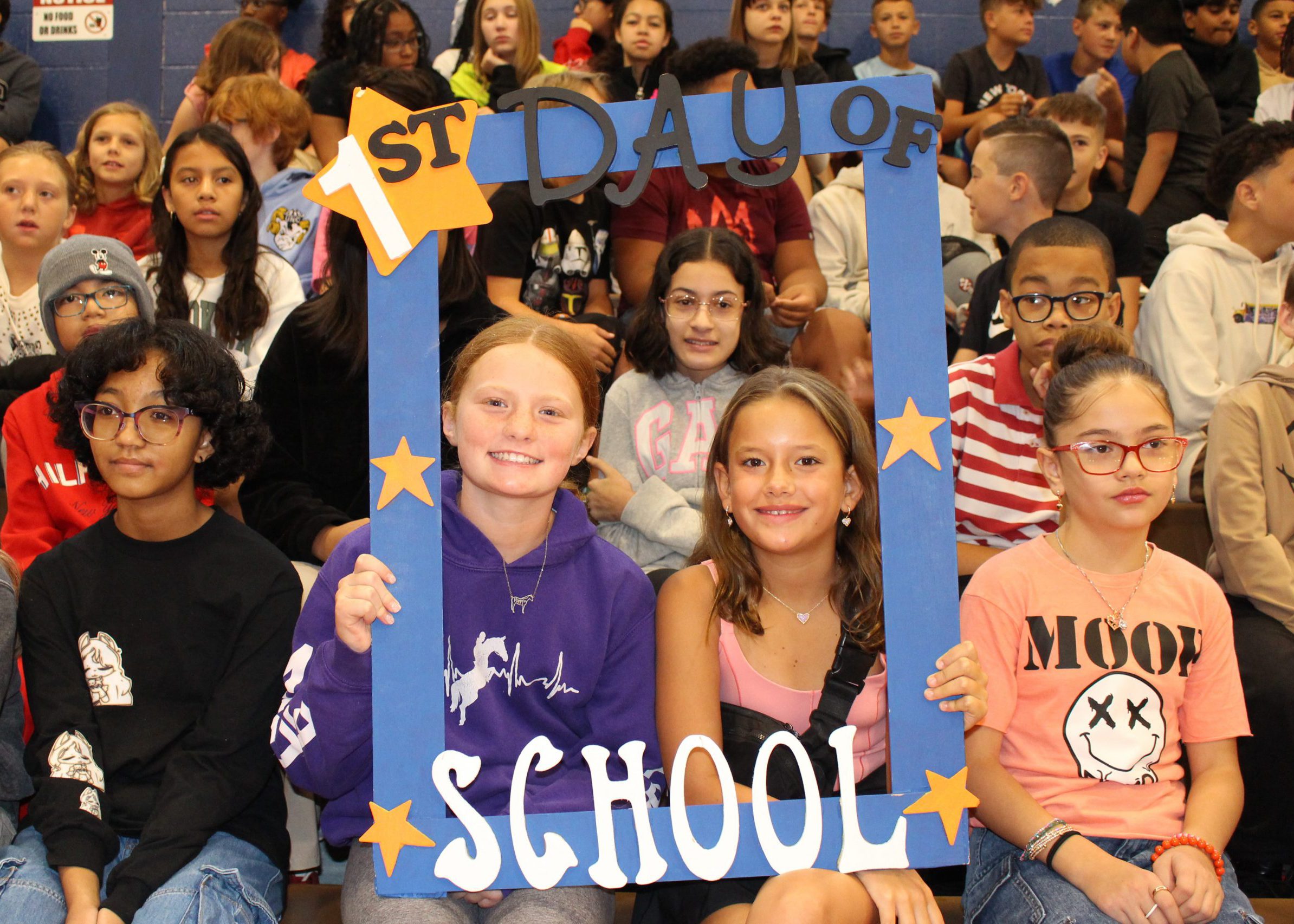 students smile from inside large frame that says "first day of school"