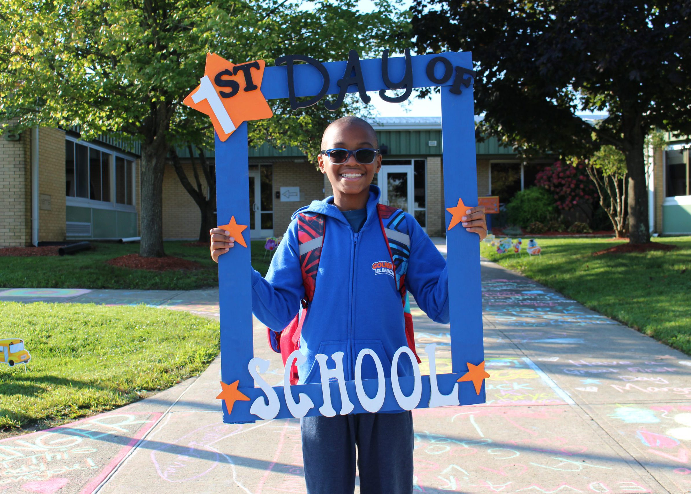 student smiles from inside large frame that says "first day of school"