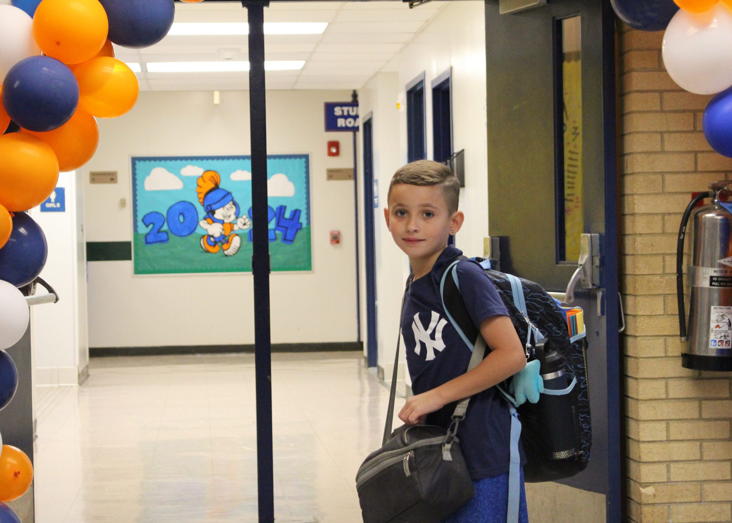 student smiles under balloon arch with his backpack