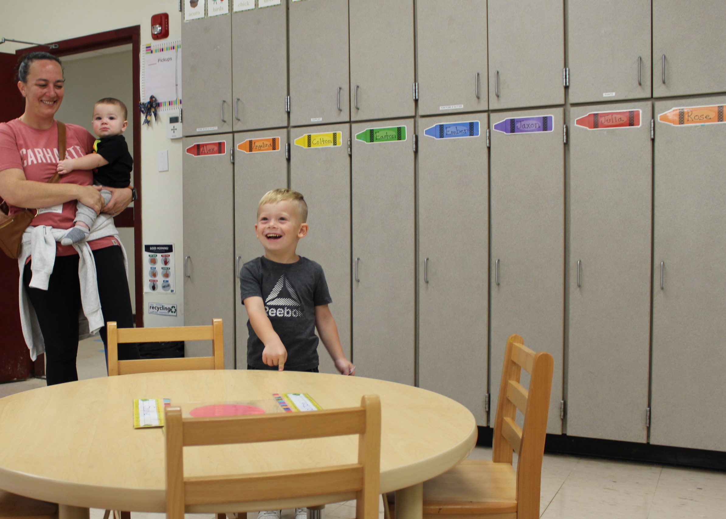 pre-k student smiles and points as he discovers his name on the table