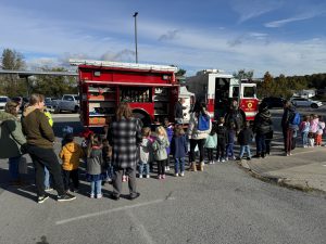 a class of students stands in front of a fire truck learning about fire safety from a firefighter