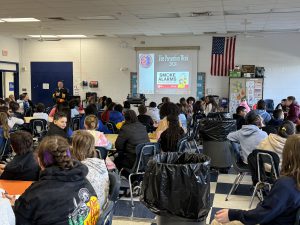 fourth and fifth grade students sit in the cafeteria and hear about fire safety from a firefighter